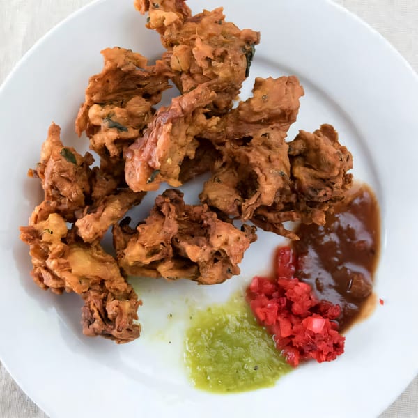 Crispy Indian pakora with green chutney, red relish, and brown sauce on a white plate.