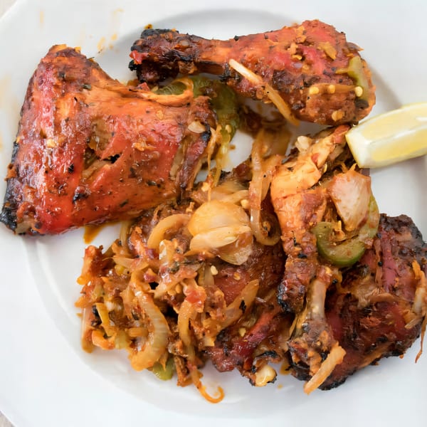 New Taj Mahal's Indian tandoori chicken with onions, peppers, and a lemon wedge on a white plate.
