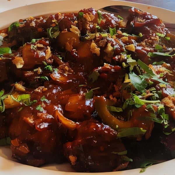 Close-up of a New Taj Mahal Indian dish with dark sauce, green herbs, and fried onions.